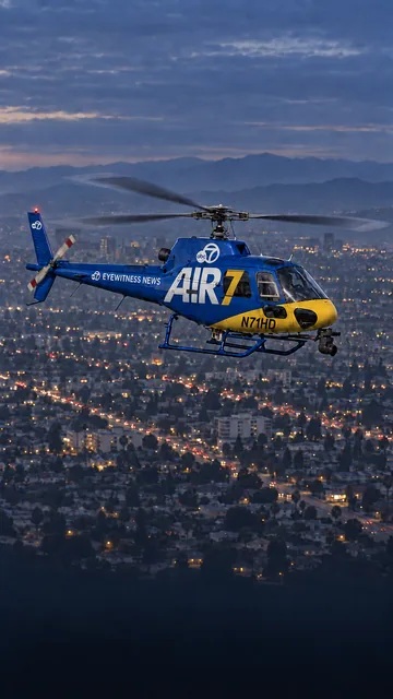 Illustration of AIR7, KABC's blue and yellow Airbus AS350 news helicopter, registration N71HD, over the Los Angeles street grid at dusk.