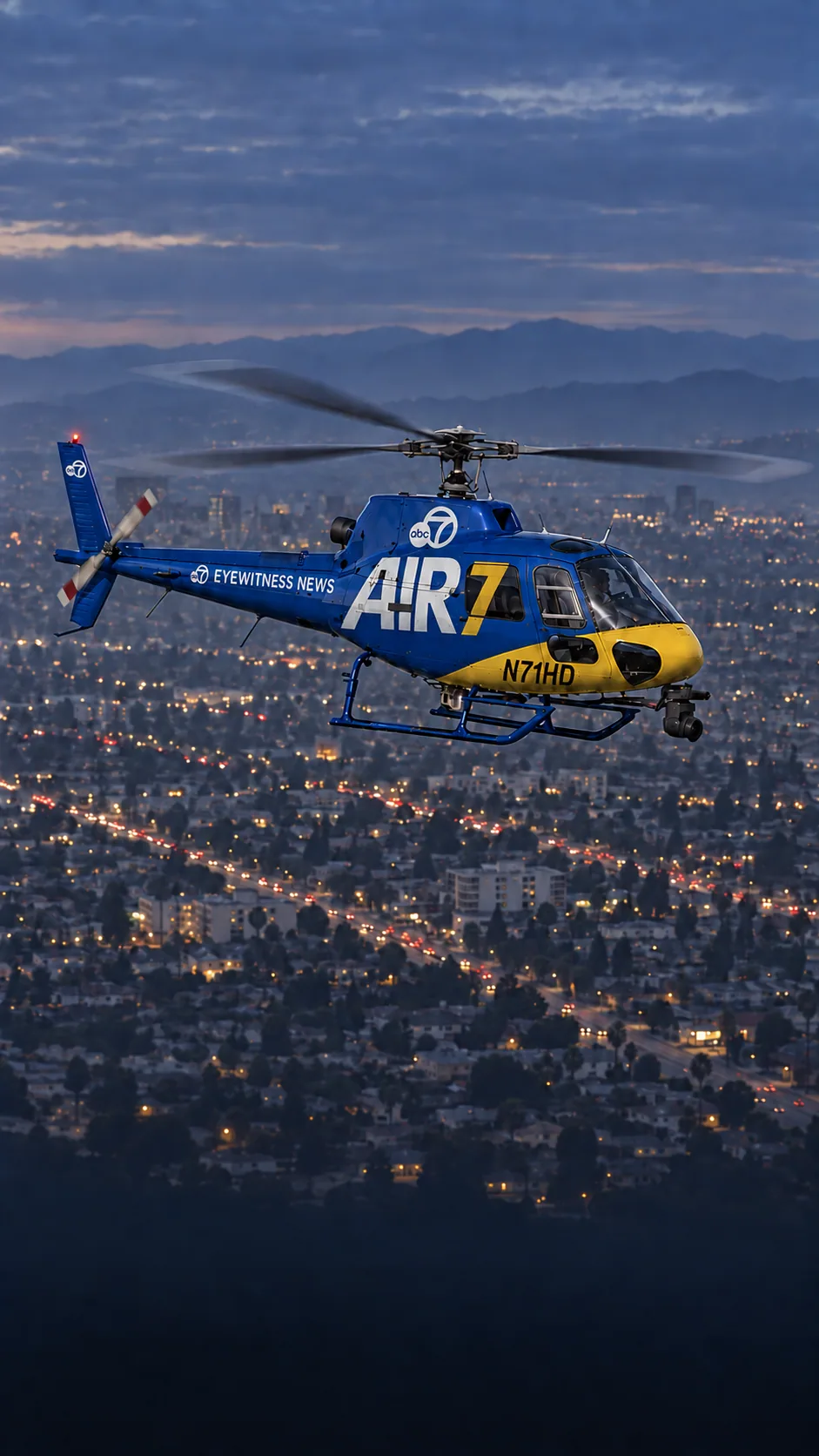 Illustration of AIR7, KABC's blue and yellow Airbus AS350 news helicopter, registration N71HD, over the Los Angeles street grid at dusk.