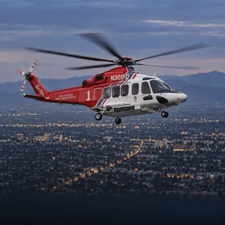 Illustration of Fire 1, the Los Angeles Fire Department's red and white Leonardo AW139, registration N301FD, over Los Angeles at dusk.