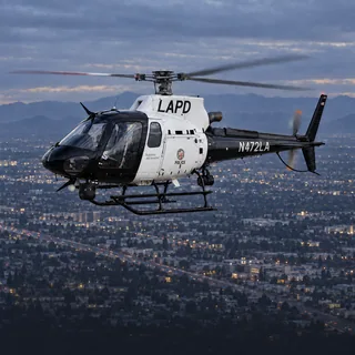 Illustration of an LAPD Air Support Division Airbus AS350 in black and white livery, registration N472LA, over Los Angeles at dusk.