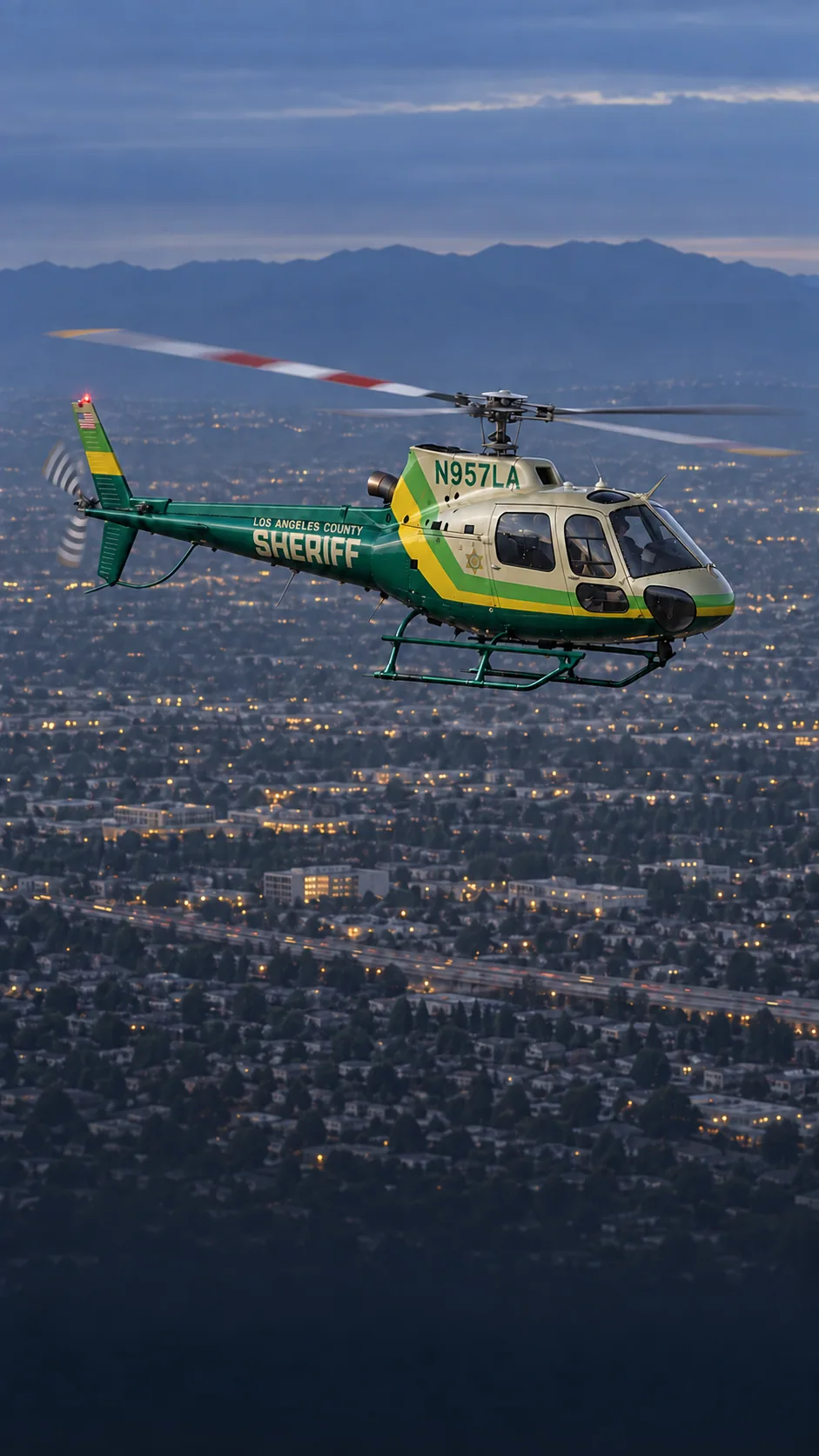Illustration of a Los Angeles County Sheriff's Department patrol Airbus AS350 in green and cream, registration N957LA, over Los Angeles at dusk.