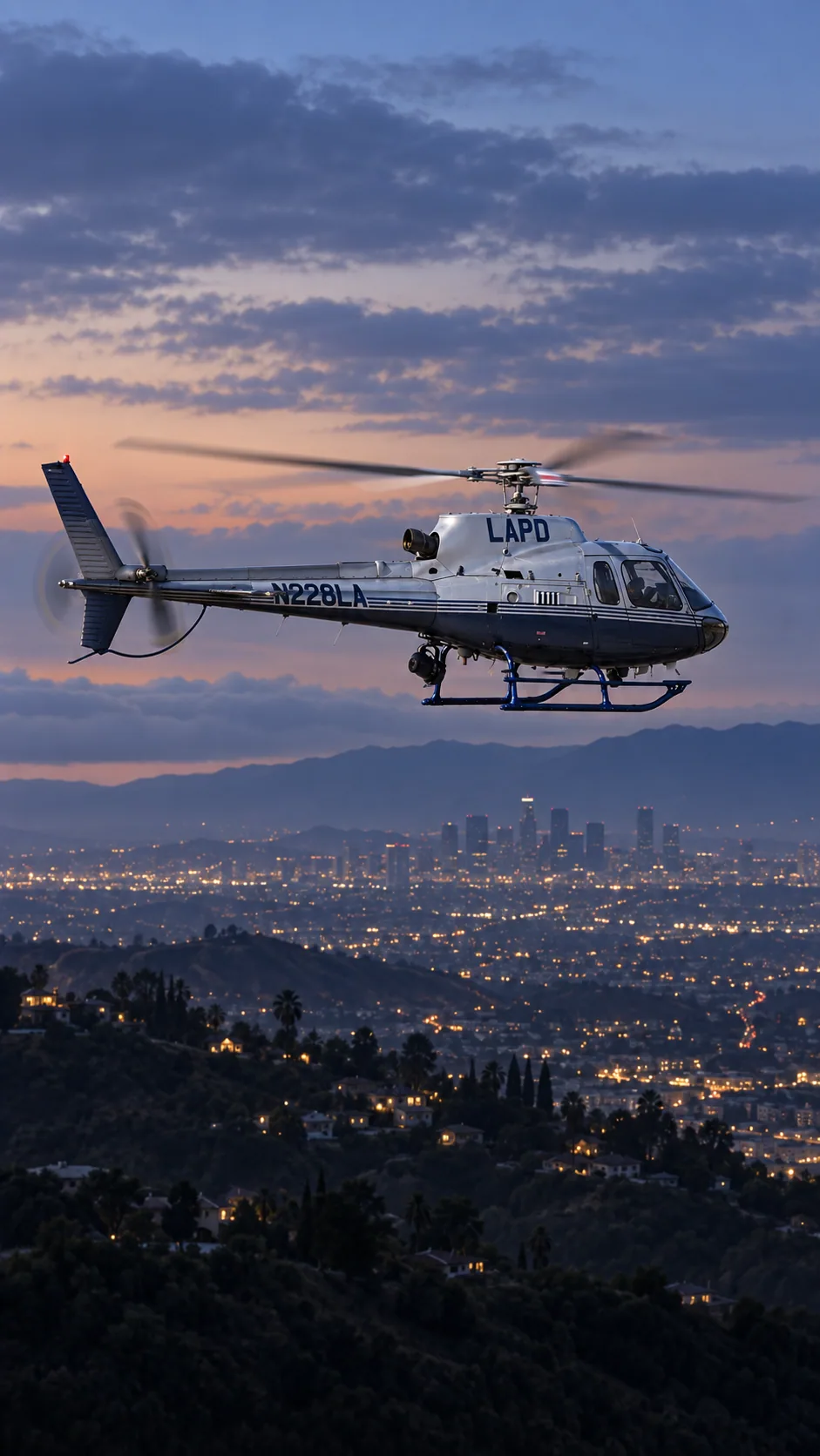 Illustration of N228LA, an Airbus AS350 B2 of LAPD Air Support — older LAPD silver-grey upper fuselage, dark navy belly, fine horizontal stripes, navy LAPD on cowling and N228LA on tail, blue skids — over the Los Angeles basin at dusk.