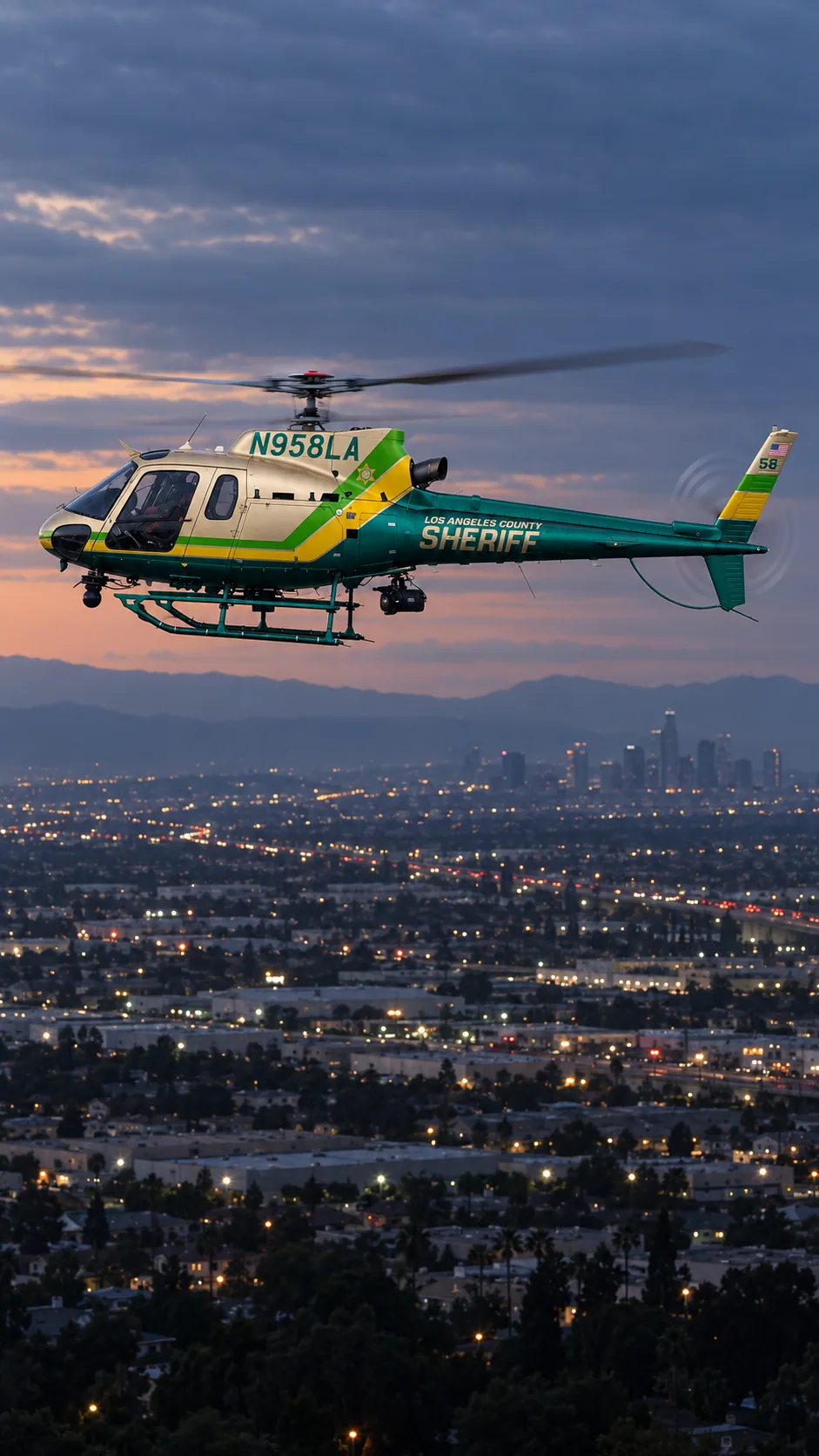 Illustration of N958LA, an Airbus AS350 B2 of Sheriff Air Support — metallic champagne/gold cabin, emerald green tail and belly, lime green and yellow diagonal bands — over the Los Angeles basin at dusk.