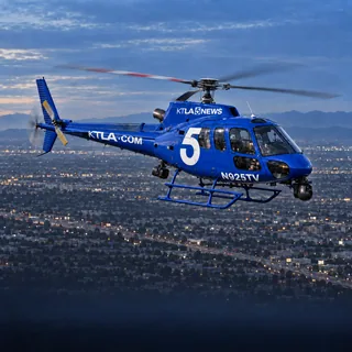 Illustration of Sky5, KTLA's royal-blue Airbus AS350 news helicopter with a large white 5, registration N925TV, over Los Angeles at dusk.