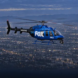 Illustration of the shared SkyFOX 11 / SkyCAL Bell 407 news helicopter, registration N50Q, showing its blue and black SkyFOX side over Los Angeles at dusk.